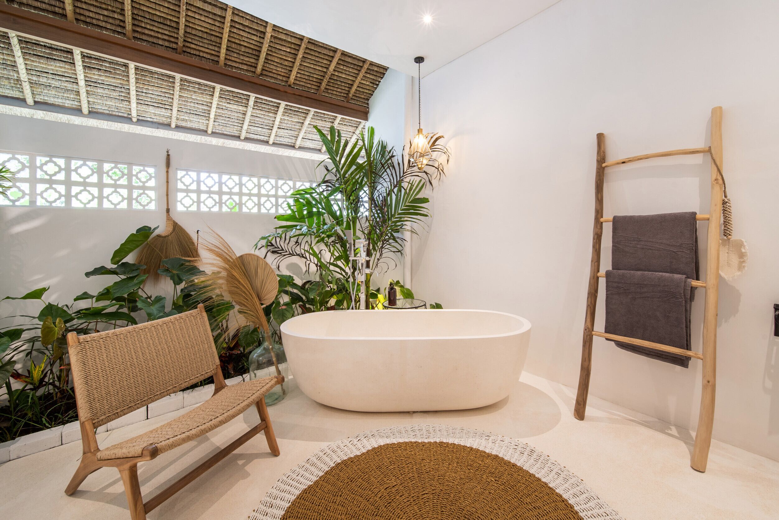 A modern bathroom with a large bathtub, a wooden bench, and a ladder for hanging towels.