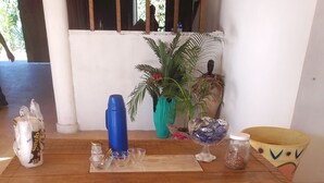 A wooden dining table with a woven pattern, surrounded by various items including a blue vase, a green plant, and a yellow bowl. - Ebora Pousada (Ilhéus)