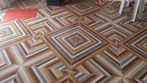 A room with a geometric patterned floor, a mirror on the wall, a small black object on the floor, and a white chair. - Ebora Pousada (Ilhéus)