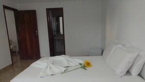 A neatly made bed with white linens and a single yellow flower. - Ebora Pousada (Ilhéus)