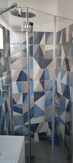 Una doccia con porta in vetro, decorata con un motivo a piastrelle geometriche, e un soffione a mano.