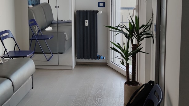 A modern living room with a grey sofa, a blue chair, a radiator, a potted plant, and a sliding glass door leading to another room. - Appartamento Lucerelaxcomfort - Studio Flat (Milan)
