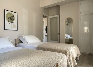 A hotel room with two beds, a wardrobe, a mirror, and a framed artwork on the wall.