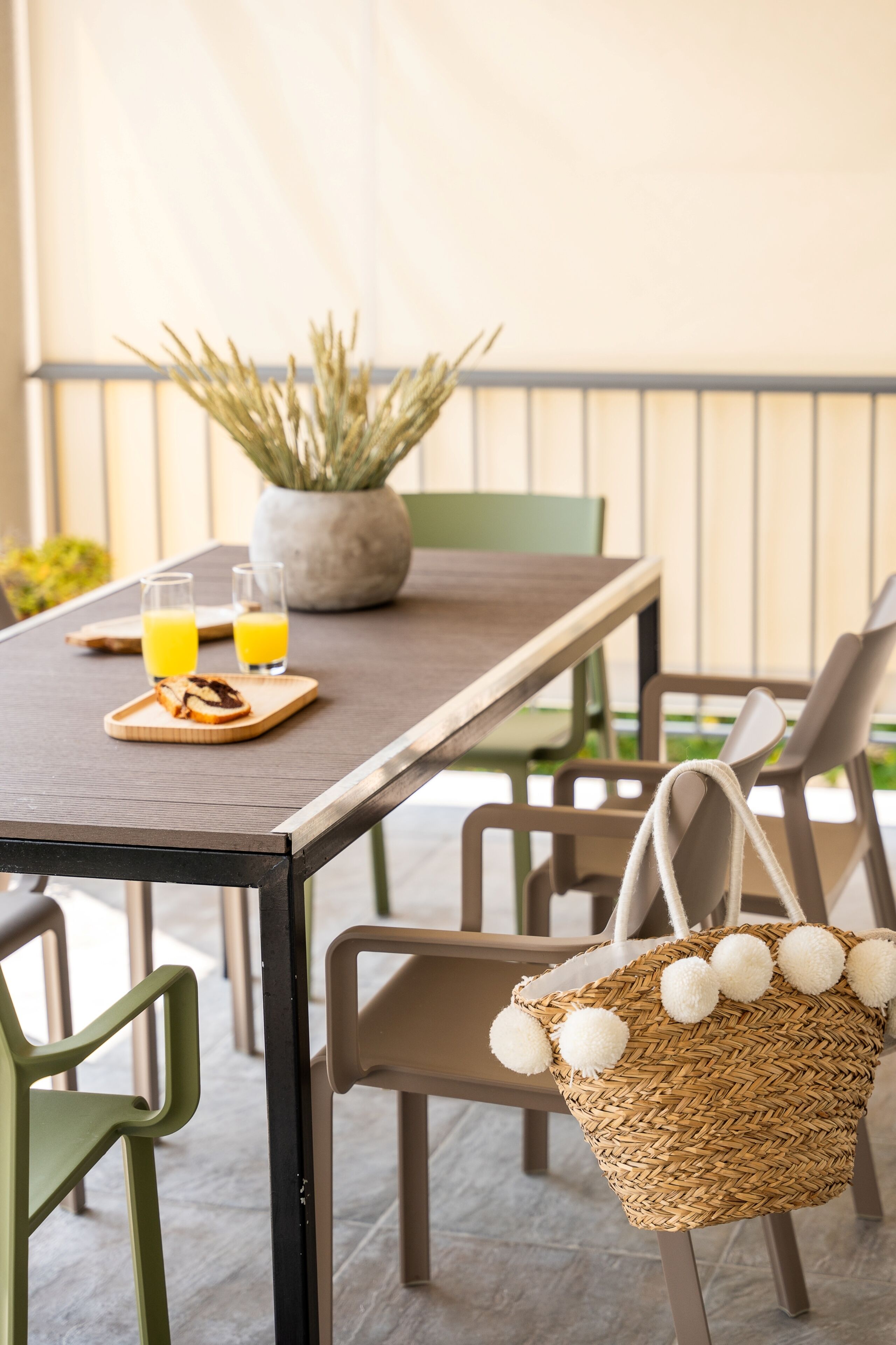 A dining table with two glasses of orange juice, a potted plant, and a wicker basket with pom-poms.