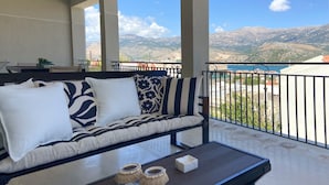 Ein Balkon mit einer Couch und einem Tisch, der Blick auf Berge und ein Gewässer bietet.