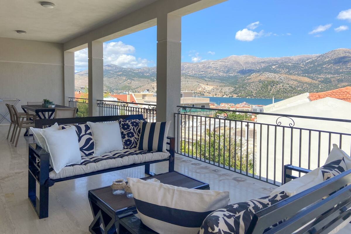 Un balcon aménagé avec un canapé, des chaises et une table. Il offre une vue sur un paysage montagneux et une étendue d’eau.