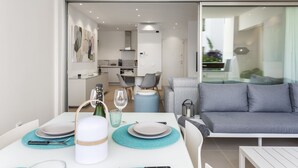 A modern dining area with a table set for two, a sofa, and a kitchen in the background. - Luxury apartment: air conditioning, swimming pools, heating, gym, fibre optics, garage (Palm-Mar)
