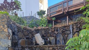 A stone retaining wall with a small waterfall, surrounded by lush greenery and a wooden bridge. - Luxury apartment: air conditioning, swimming pools, heating, gym, fibre optics, garage (Palm-Mar)