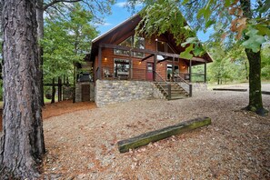 A rustic cabin with a stone foundation, wooden exterior, and a porch with a staircase leading to the entrance.