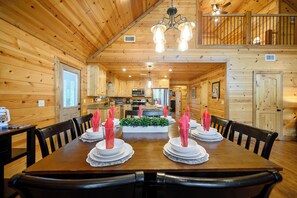 L’intérieur d’un chalet en bois comprend une salle à manger avec une table dressée pour quatre personnes, un coin cuisine et un balcon.