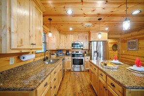 A wooden cabin interior with a kitchen featuring granite countertops, stainless steel appliances, and wooden cabinets.