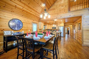 A wooden interior with a dining area, a clock, and a kitchen.