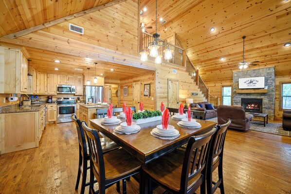 Une cabane en bois spacieuse comprenant un coin repas aménagé pour les repas, une cuisine, un salon et une cheminée.