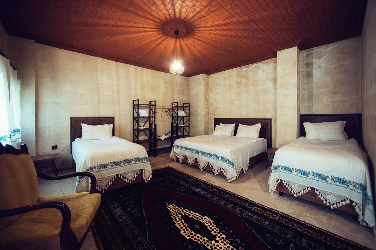 A hotel room with three beds, a wooden ceiling, and a traditional rug.