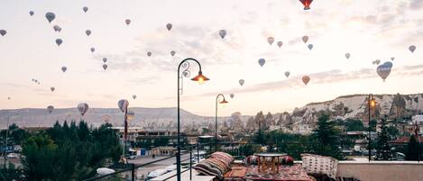 A rooftop terrace with a view of a cityscape and mountains, featuring a table and chairs set up for dining.