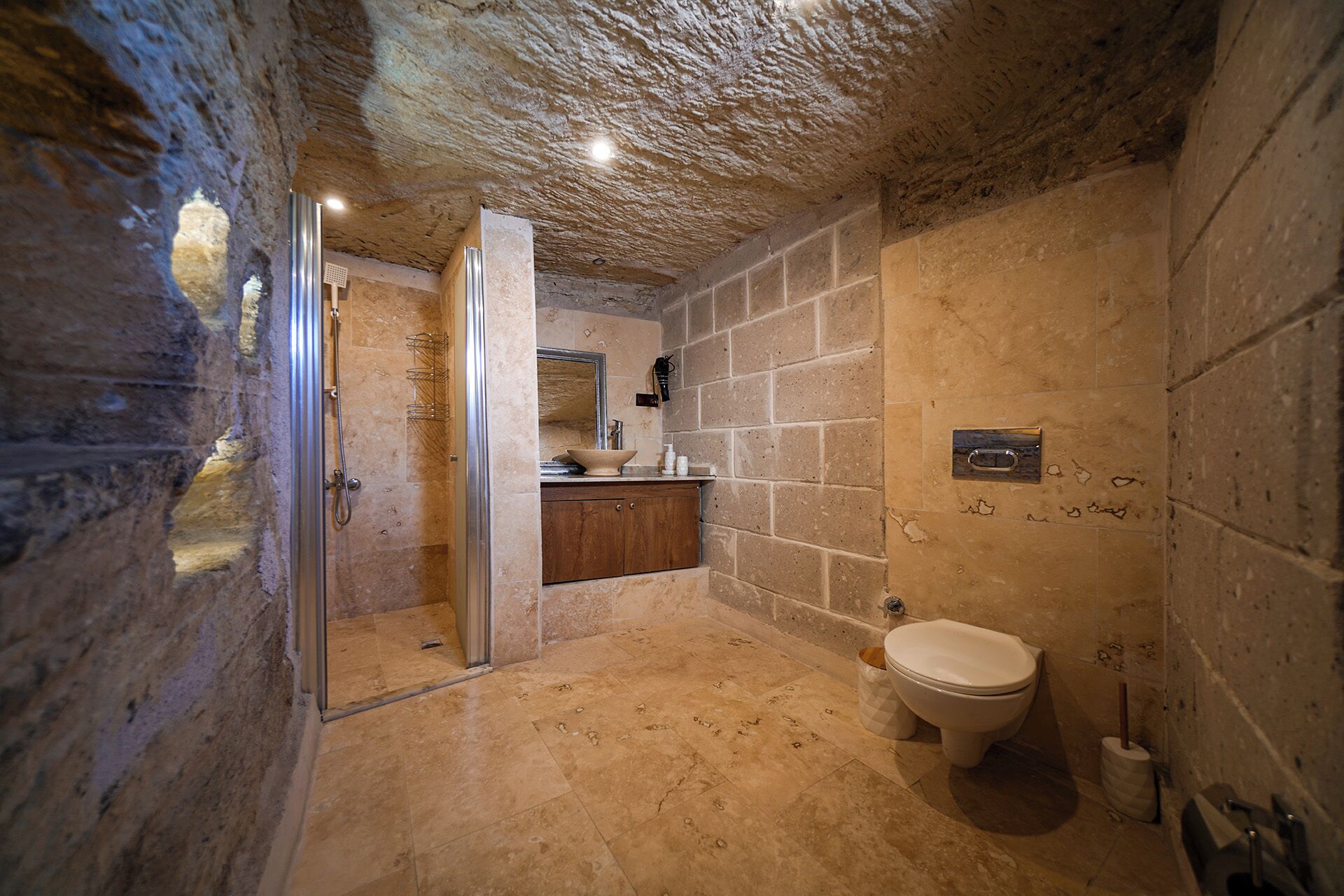 A bathroom with a stone wall, a toilet, a sink, and a shower area.