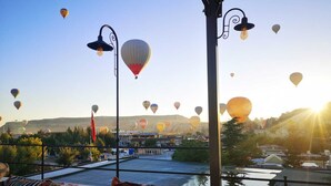 A rooftop terrace with a view of hot air balloons in the distance, a patterned cushion, and a street lamp. - Azalea Terrace Cave Hotel (Nevsehir)