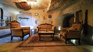 A cozy room with a fireplace, two armchairs, a sofa, and a patterned rug. - Azalea Terrace Cave Hotel (Nevsehir)