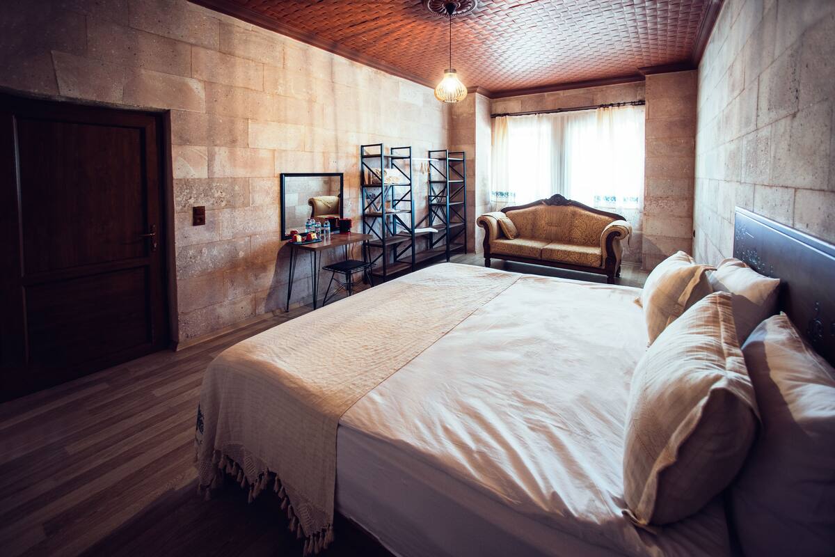A bedroom with a large bed, a wooden ceiling, a stone wall, a wooden door, and a window with curtains.