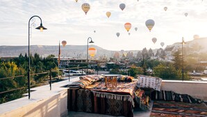A rooftop terrace with a view of a city and mountains, featuring a sofa, a table, and a lamp. - Azalea Terrace Cave Hotel (Nevsehir)