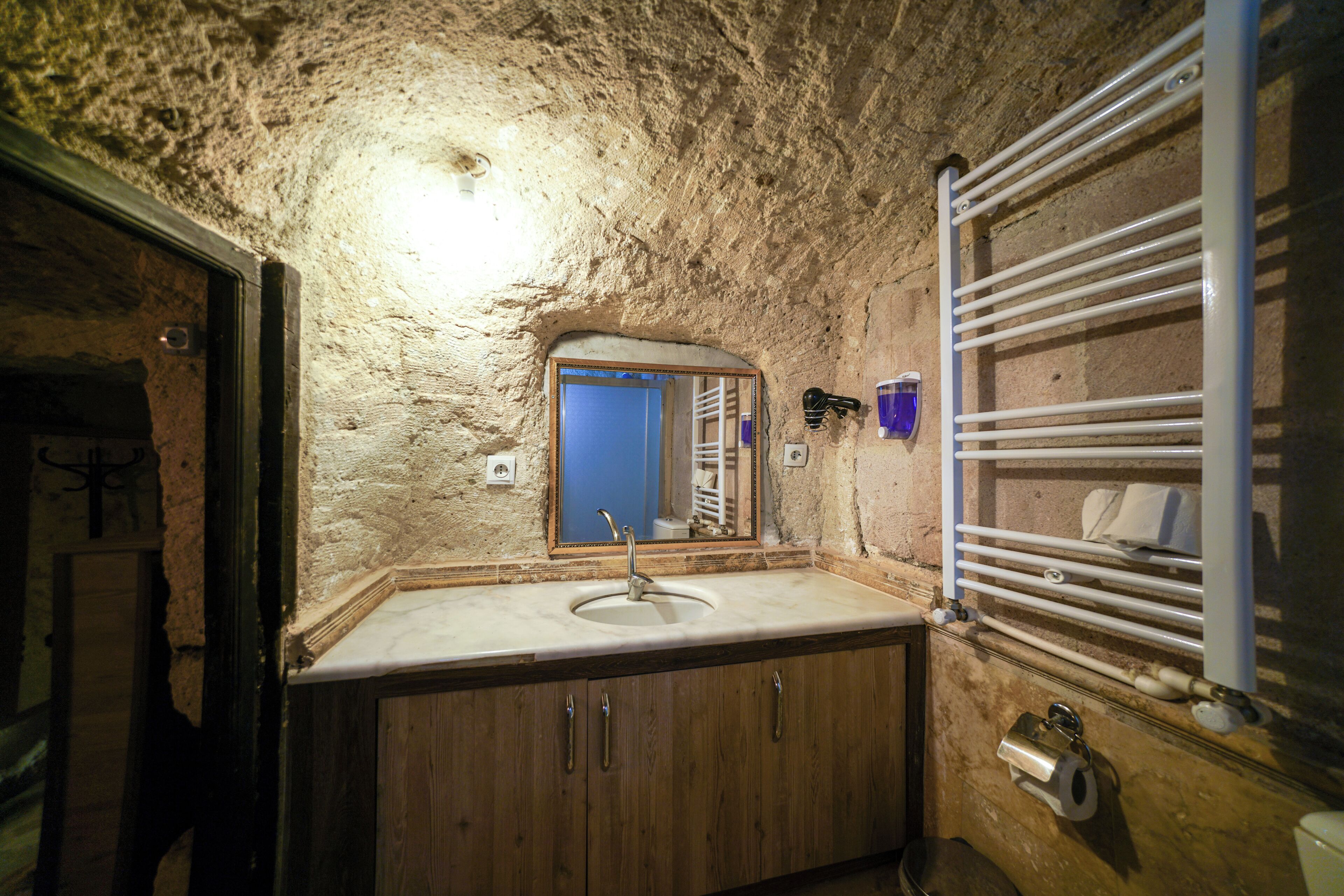 A bathroom with a stone wall, wooden cabinets, a sink, a mirror, and a towel rack.