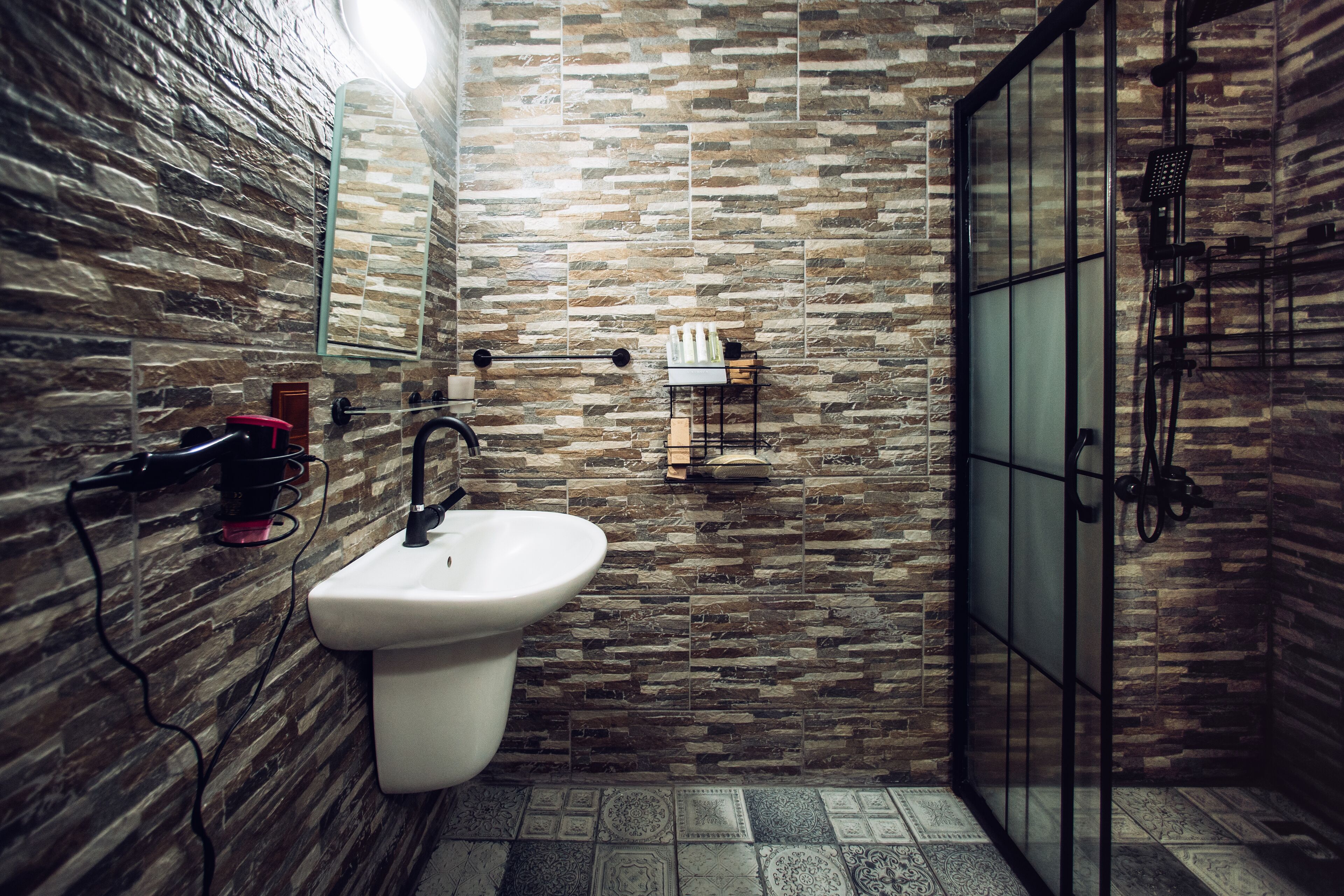 Un baño con pared de piedra, un lavabo blanco y una cabina de ducha de vidrio.