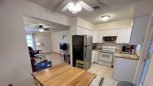 A compact kitchen with white cabinets, a black refrigerator, a stove, and a microwave. There is a dining table with chairs and a trash bin. - Close To Beach, 3Bdrm / 2 Bath Duplex (Nokomis)