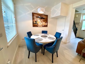 A dining area with a round table, blue upholstered chairs, and a modern pendant light. - Captivating House in Aberdare Sleeps 6 Near Brecon (Aberdare)