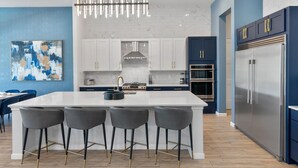 Une cuisine moderne dotée d’un îlot central, de tabourets de bar, d’appareils électroménagers en acier inoxydable et d’un mur d’accent bleu.