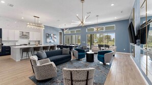A spacious living area with a sofa, chairs, a coffee table, and a TV. There is a kitchen area with a bar and seating. - Action-Packed Home w Sports Simulator, Bowling, Gamer BR & Theater - Near Parks (Davenport)