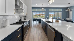 A modern kitchen with a large island, white cabinetry, and a view of the outdoors. - Action-Packed Home w Sports Simulator, Bowling, Gamer BR & Theater - Near Parks (Davenport)