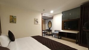 A hotel room with a large bed, a desk with a chair, a television, and a mirror. - RKN Grand Hotel (Puducherry)