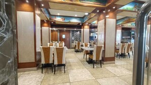 A restaurant with multiple dining tables and chairs, a tiled floor, and a mural on the ceiling. - RKN Grand Hotel (Puducherry)