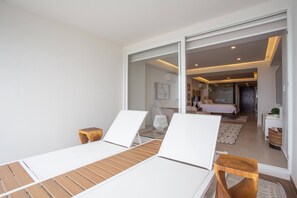 A modern bedroom with a large bed, a desk, and a chair. There is a sliding door leading to a bathroom.