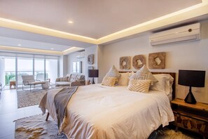A modern bedroom with a large bed, a sitting area with a chair and a table, and a view through large windows.