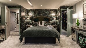 Una habitació àmplia amb un llit gran, dues taules de nit, una estanteria i un mirall.