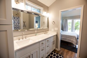 A bathroom with a double sink, a large mirror, and a shower with blue tiles. - Cozy, lake front cottage (Lyman)