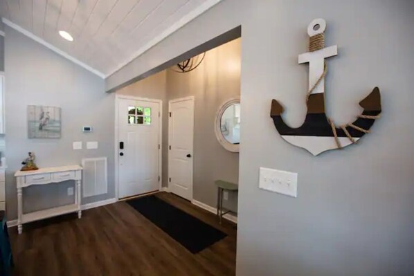 A hallway with a wooden floor, a white console table, a round mirror, and a wall-mounted anchor decoration. - Cozy, lake front cottage (Lyman)