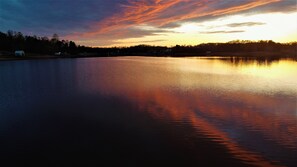 A calm lake at sunset with a clear sky and distant buildings. - Cozy, lake front cottage (Lyman)