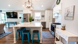 A modern kitchen with a central island, bar stools, a built-in oven, and a dining area with a sofa and coffee table.