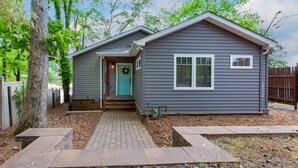 A single-story house with a front porch, a door with a wreath, and a small front yard with a tree and a fence.