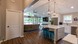 A spacious kitchen with a large island, bar stools, and a ceiling fan.