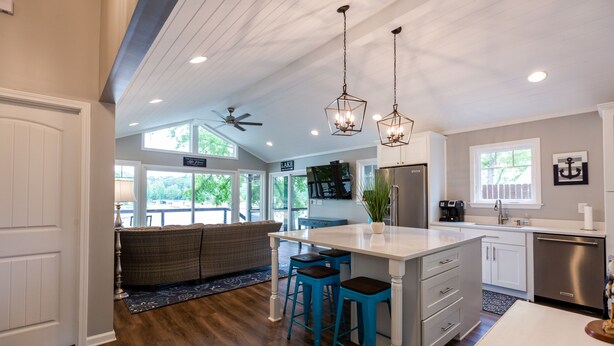 A modern kitchen with a central island, bar stools, and a ceiling fan.