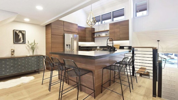 Una cocina moderna con una isla central, taburetes de bar y una lámpara colgante.