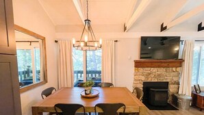 A dining area with a wooden table, chairs, a chandelier, a stone fireplace, and a TV mounted above it. - Seasons 4 #140- Close to Canyon Lodge & The Villag (Mammoth Lakes)