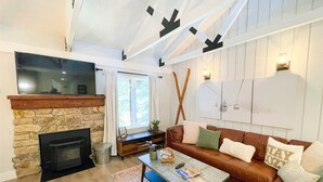 A living room with a stone fireplace, a brown leather sofa, a coffee table, and a flat-screen TV mounted on the wall. - Seasons 4 #140- Close to Canyon Lodge & The Villag (Mammoth Lakes)