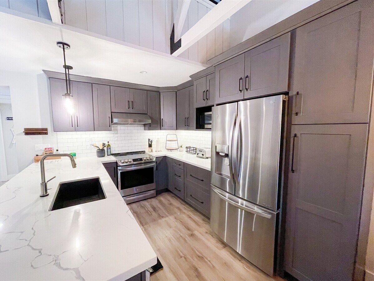 A modern kitchen with grey cabinets, stainless steel appliances, and a white countertop.