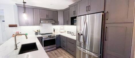 A modern kitchen with grey cabinets, stainless steel appliances, and a white countertop.