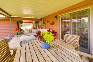Un patio coperto con mobili in legno, una pianta in vaso blu e un cartello con la scritta 'stay awhile'.