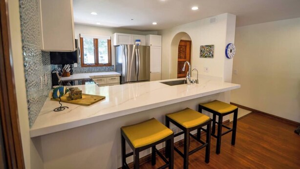 A modern kitchen with a white countertop, stainless steel appliances, and a bar area with stools. - Oceanfront view, plus corner patio and golf cart (Avalon)
